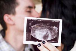 expectant partents kissing while holding up an ultrasound picture