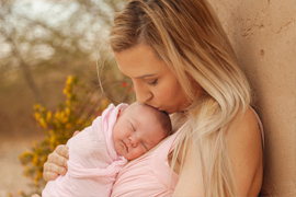 outdoor image of mom kissing newborn girl resting on her chest