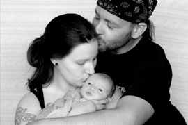 new dad kissing Mom's head while she kisses newborn baby's forehead