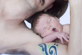 newborn boy yawning while resting on dad's bicept with a g-cleff tattoo
