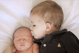  older brother kissing newborn girl photographed from above